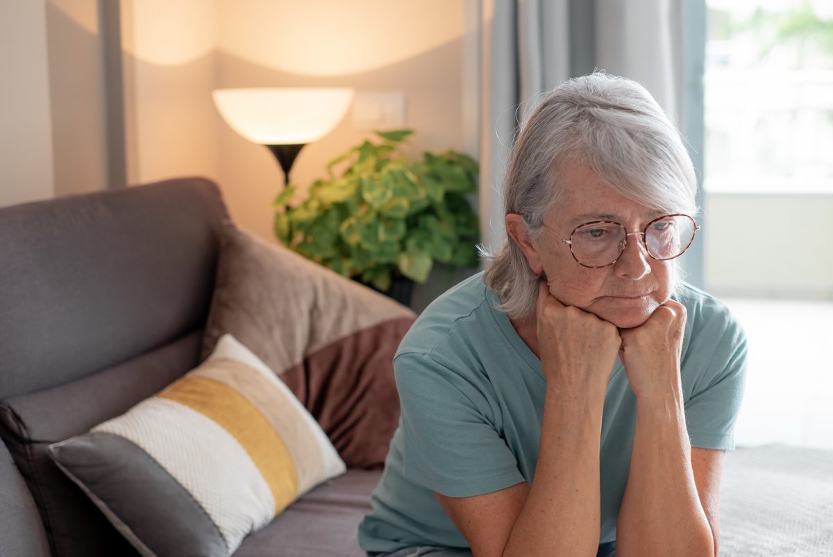 Ältere Frau sitzt nachdenklich auf dem Sofa